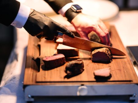 Anrichten Ein Koch schneidet Fleisch auf einem Holzbrett mit einem großen Messer.
